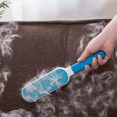 A blue pet hair remover brush lifting loose fur from a dark fabric sofa, showing collected pet hair on the brush surface.