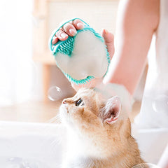 Cat being washed with a turquoise silicone grooming brush during bath time.
