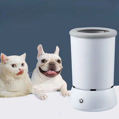 A white USB rechargeable automatic dog and cat paw washer with soft silicone bristles, shown beside a dog and a cat on a solid background.